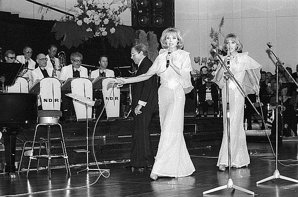 Die "Kessler-Zwillinge" am 23. Oktober 1976 mit dem Tanzorchester des "Norddeutschen Rundfunks" (NDR) unter Leitung von Franz Thon anl�sslich eines Wohlt�tigkeitsballs des "Deutschen Roten Kreuzes" (DRK) im "Kieler Schloss"; Urheber: Friedrich Magnussen (1914�1987); Lizenz: CC BY-SA 3.0 DE; Rechteinhaber: "Gesellschaft f&uuml;r Kieler Stadtgeschichte", Bildnachlass Friedrich Magnussen (ID-Nummer: 68.396); Quelle: Wikimedia Commons von "Stadtarchiv Kiel"