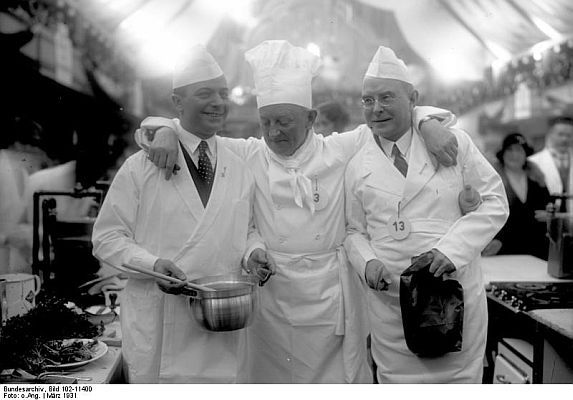 Prominente Bühnen- und Filmschauspieler als Kochkünstler auf der Kochkunstausstellung am Kaiserdamm! Ein lustiges Trio, die Filmschauspieler PaulHeidemann1) (links), OttoGebühr2) (Mitte) und WilhelmBendow (rechts) auf der Kochkunstausstellung (März1931). Quelle: Deutsches Bundesarchiv, Digitale Bilddatenbank, Bild 102-11400; Fotograf: unbekannt / Datierung: März 1931 / Lizenz CC-BY-SA 3.0.