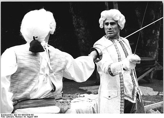 Foto: Gojko Mitic 1984 bei einer Fechtprobe im "Bergtheater Thale"; Quelle: Deutsches Bundesarchiv, Digitale Bilddatenbank, Bild 183-1984-0810-302; Urheber: Lehmann, Thomas / Datierung: 10. August 1984 / Lizenz CC-BY-SA 3.0 DE; Originalfoto und Beschreibung: Deutsches Bundesarchiv Bild 183-1984-0810-302; bzw. Wikimedia Commons 