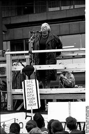 Steffie Spira spricht am 4. November 1989 auf dem "Alexanderplatz"; Quelle: Deutsches Bundesarchiv, Digitale Bilddatenbank, Bild 183-1989-1104-049; Fotograf: Huvert Link / Datierung: 04.11.1989 / Lizenz CC-BY-SA 3.0.; Originalfoto und Beschreibung: Deutsches Bundesarchiv Bild 183-1989-1104-049 bzw. Wikimedia Commons