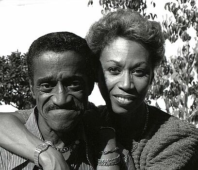 Sammy Davis jr. mit seiner Frau Altovise 1986 in seinem Heim in Beverly Hills; Quelle: commons.wikimedia.org bzw. Wikipedia; Urheber: Allan Warren (www.allanwarren.com); Diese Datei ist unter der Creative Commons-Lizenz Namensnennung-Weitergabe unter gleichen Bedingungen 3.0 Unported lizenziert. Es ist erlaubt, die Datei unter den Bedingungen der GNU-Lizenz für freie Dokumentation, Version 1.2 oder einer späteren Version, veröffentlicht von der Free Software Foundation, zu kopieren, zu verbreiten und/oder zu modifizieren; es gibt keine unveränderlichen Abschnitte, keinen vorderen und keinen hinteren Umschlagtext. Der vollständige Lizenztext ist im Kapitel GNU-Lizenz für freie Dokumentation verfügbar.