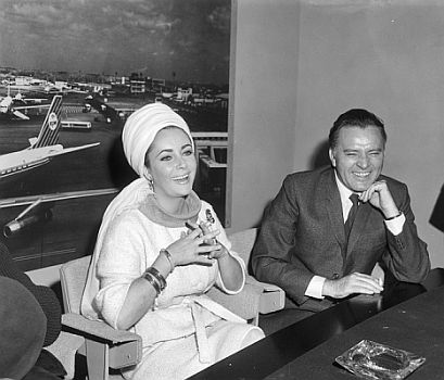 Richard Burton und Elizabeth Taylor am 26. April 1965 am "Flughafen Schiphol" in Amsterdam; Rechteinhaber: Nationaal Archief (Den Haag, Rijksfotoarchief; Bestandsnummer: 917-6934); Urheber/Fotograf: Joop van Bilsen / Anefo; Quelle: Wikimedia Commons; Lizenz: CC0 1.0 (Kein Urheberrechtsschutz)