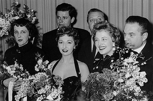 Gruppenfoto anlässlich einer Vorstellung (1955) in Frankfurt/M des Films "Musik, Musik und nur Musik"; (v.l.n.r.): Inge Egger, Walter Giller, Suzi Miller, Benny de Weille (Musik), Lonny Kellner sowie Regisseur Ernst Matray; Urheber: Harald-Reportagen (Kurt Liese (1915-2010)); Lizenz: CC BY-SA 4.0; Quelle: Wikimedia Commons