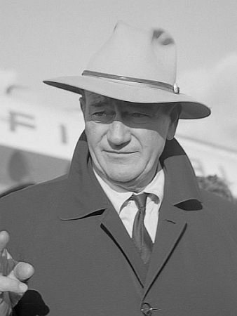 John Wayne Mitte November 1960 am Flughafen Amsterdam Schiphol; Rechteinhaber: Nationaal Archief (Den Haag, Rijksfotoarchief; Bestandsnummer: 911-7934); Urheber/Fotograf: Hugo van Gelderen / Anefo; Ausschnitt der Original-Datei; Quelle: Wikimedia Commons; Lizenz: CC BY-SA 3.0 NL